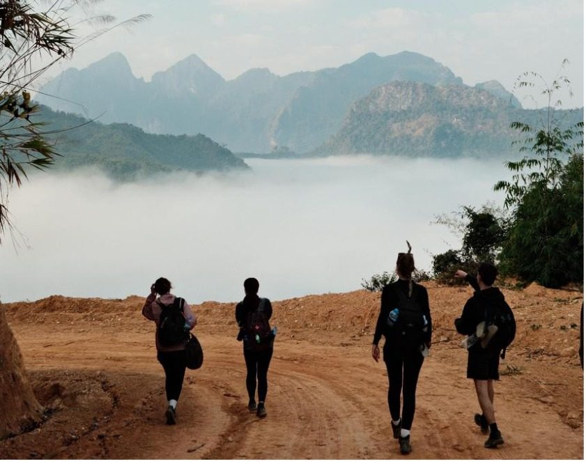 Hikers walking a dirt trail toward misty mountains