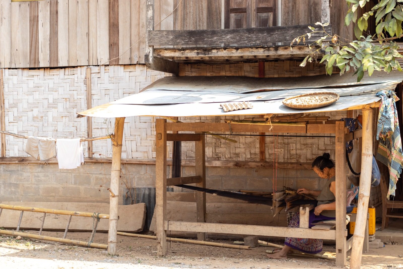 A villager weaving under a wooden house